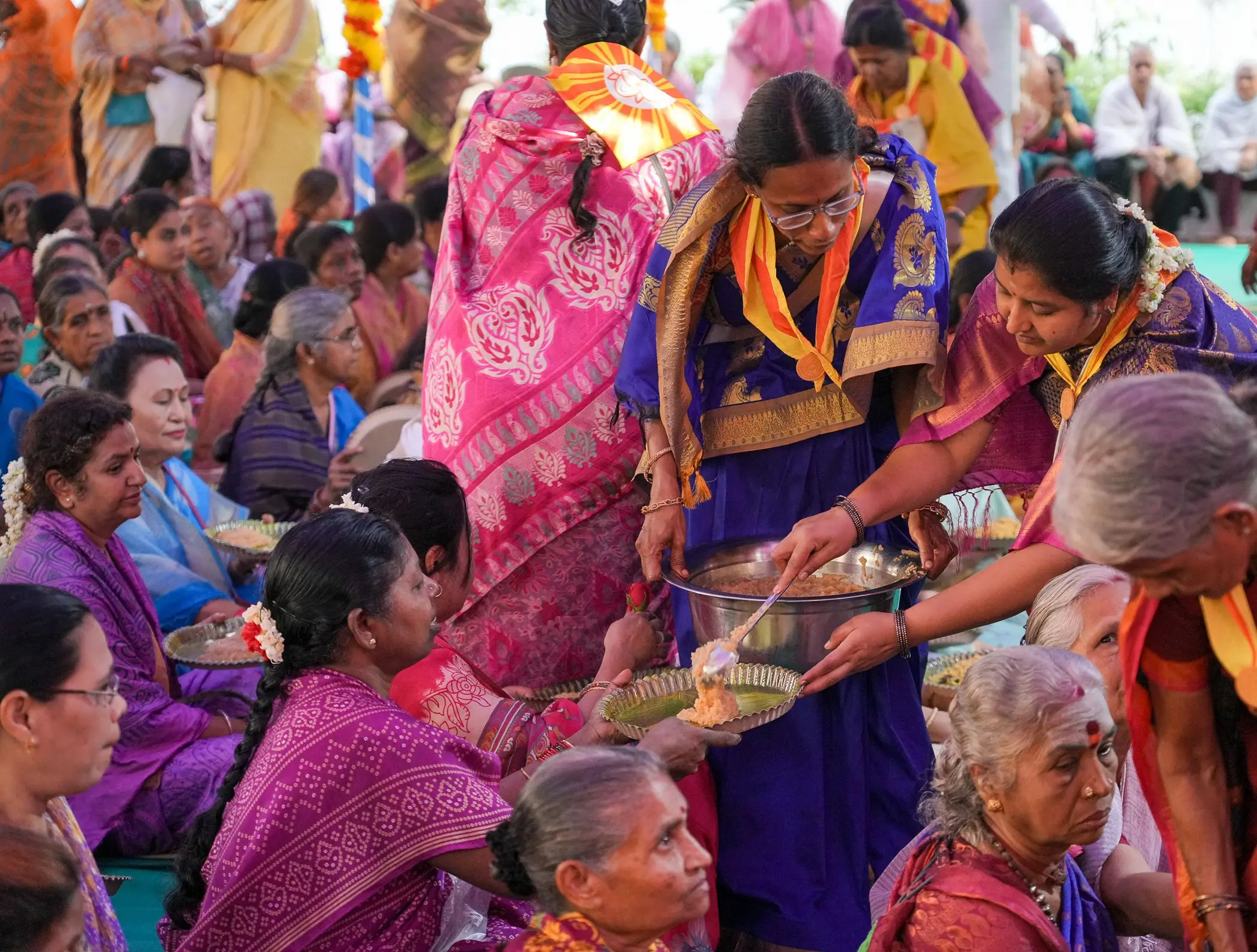 ईश्वरम्मा दिवस पर बैठी महिला भक्तों को प्रसाद परोसती महिला सेविकाएँ