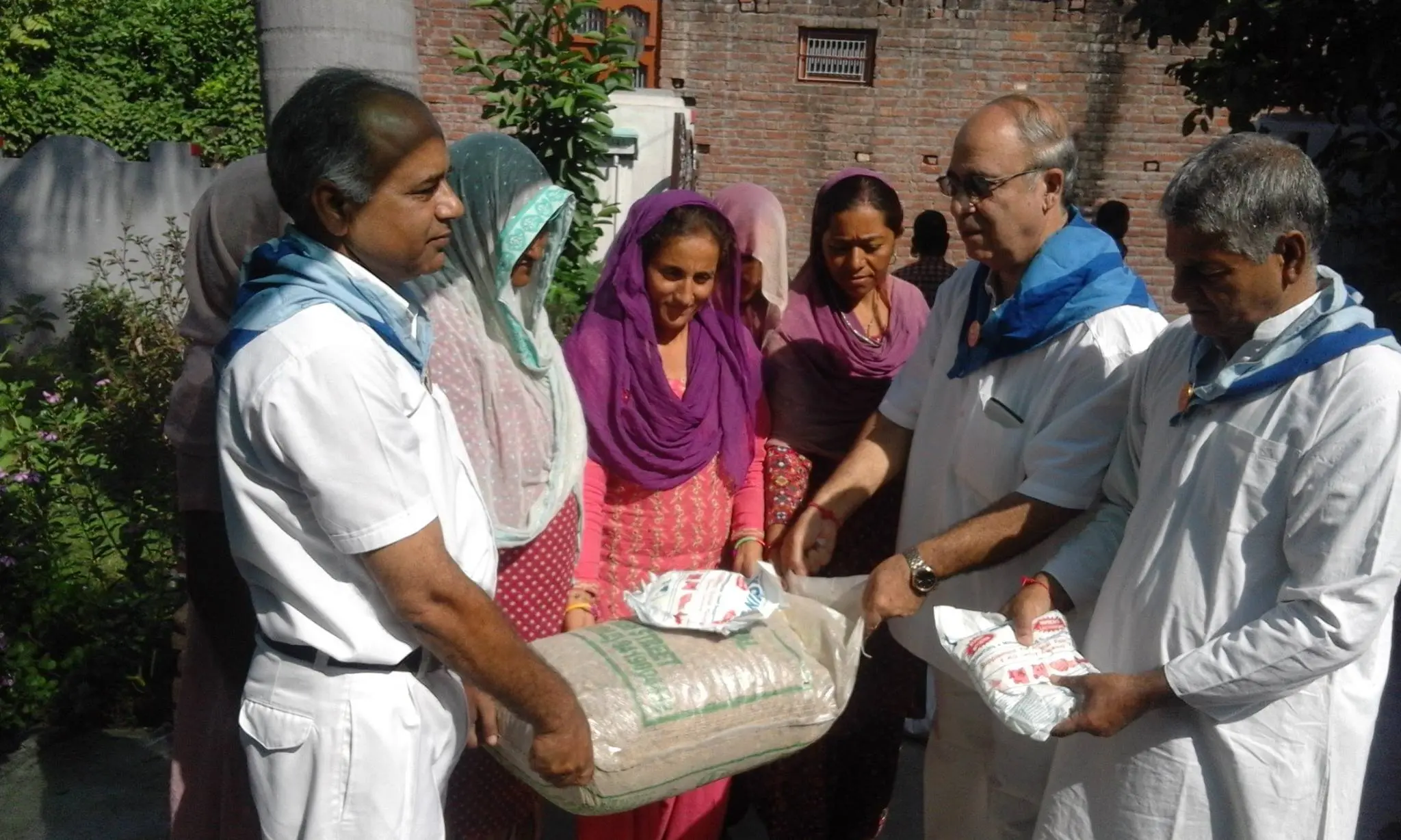 गाँव की महिलाओं को राशन के थैले सौंपते नीले स्कार्फ़ वाले सेवादल स्वयंसेवक