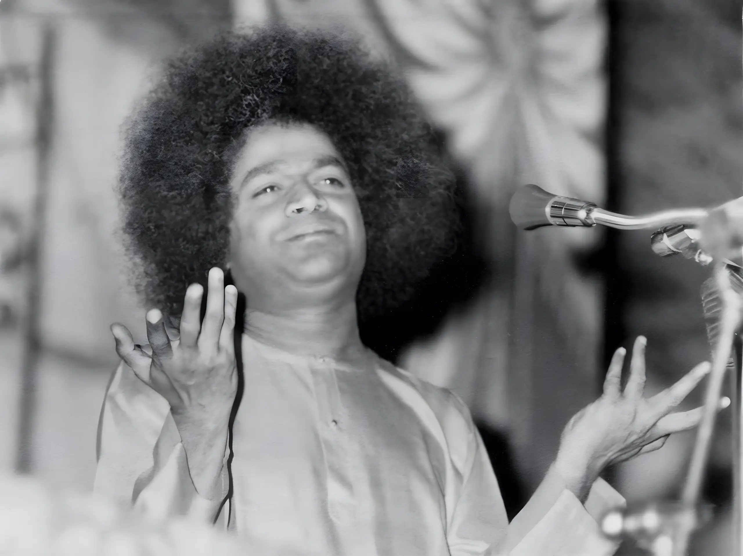 माइक्रोफ़ोन पर प्रवचन देते, हाथ उठाए भगवान श्री सत्य साई बाबा का श्वेत-श्याम चित्र