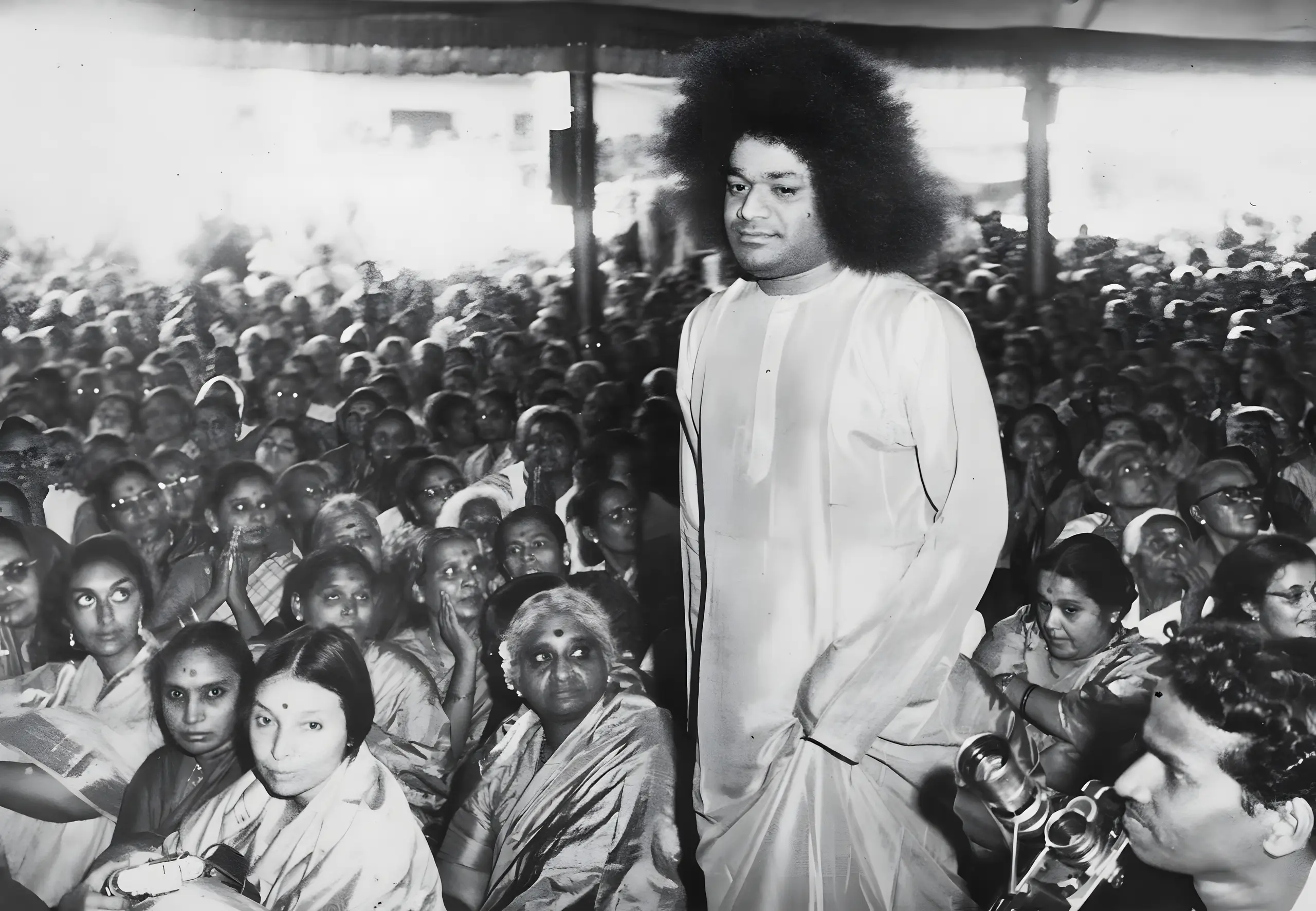 बैठे भक्तों के बीच चलते भगवान श्री सत्य साई बाबा का श्वेत-श्याम चित्र
