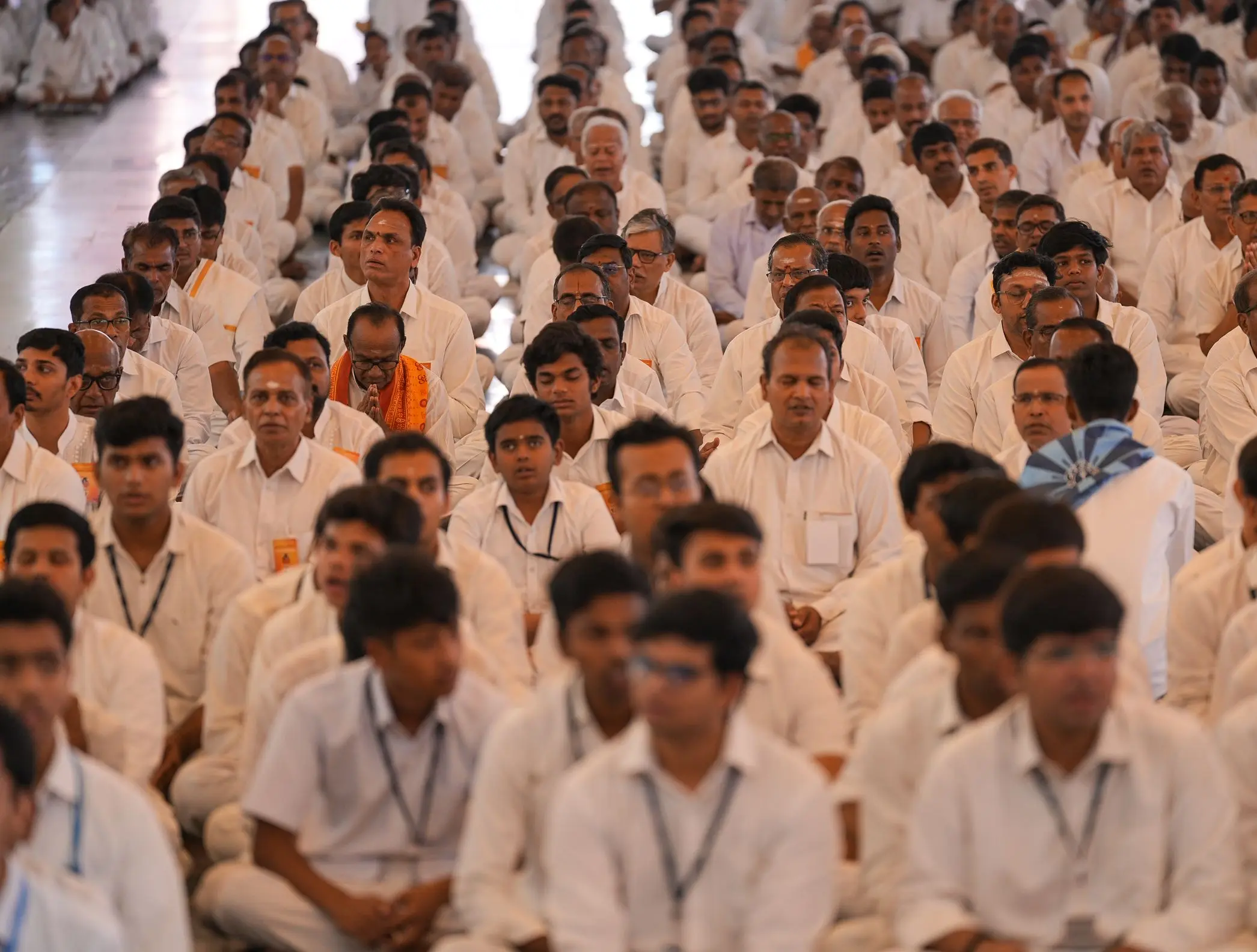 प्रशांति निलयम में वेद पाठ के दौरान पंक्तियों में बैठे सफ़ेद वस्त्रधारी पुरुष और युवा
